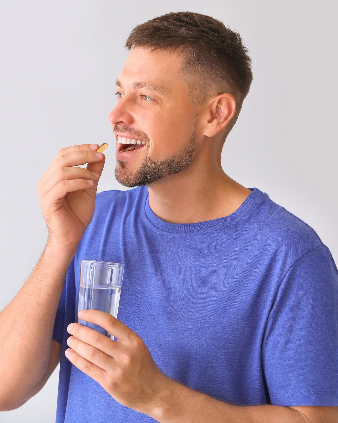 Man in blue shirt taking AminoCare supplement with a glass of water for daily wellness