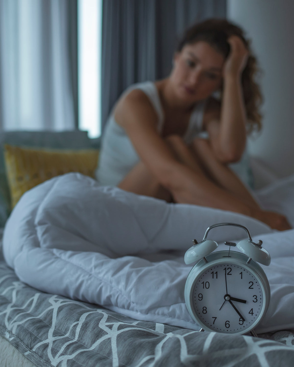 Woman sitting on bed in dimly lit room with alarm clock, promoting relaxation and magnesium support with Aminocare AminoMag