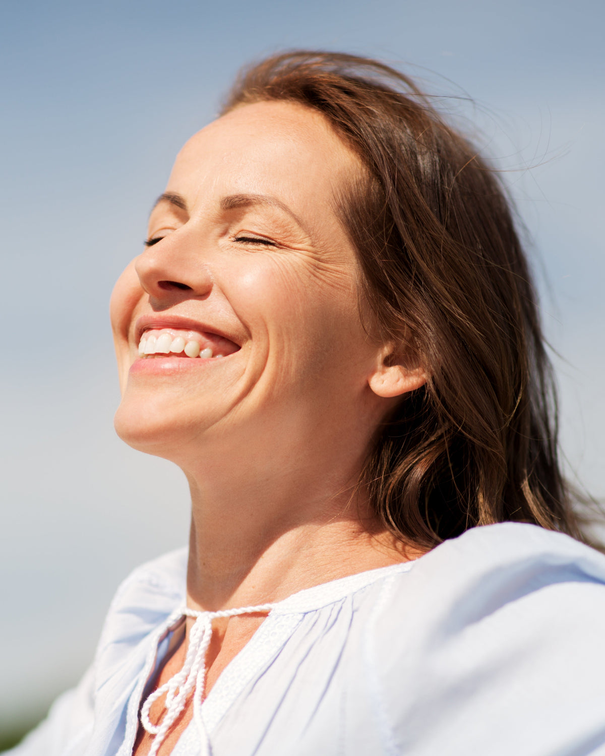 Woman smiling with sun shining on her face. Celebrating National Cancer Survivors Day with Aminocare® supplements for cellular health.